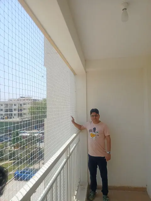 A long balcony closed from floor to ceiling with a safety net, a man standing beside it