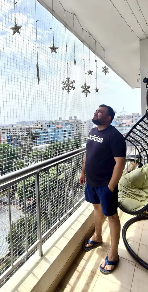 A man standing on a high-rise balcony enclosed by a full-height balcony safety net