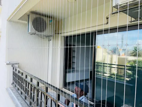 Two apartment balconies fitted with invisible grills, one beside an AC unit and one facing tall towers